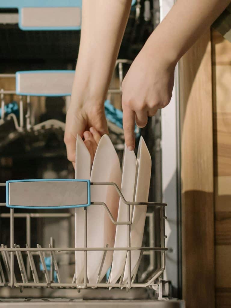 Hands loading clean dishes into an open dishwasher, demonstrating home appliance use.